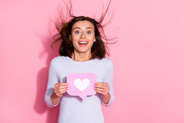 Wall Mural - Photo of carefree excited young woman wear white sweater holding notification heart like sign empty space isolated pink color background