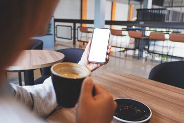 Mockup image of a woman holding mobile phone with blank desktop screen while drinking coffee