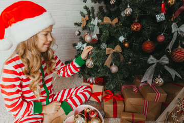 girl 9 years old in striped pajamas decorates a Christmas tree in a beautiful living room. Christmas Eve.