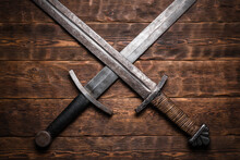 Two Crossed Swords On The Old Wooden Table Flat Lay Background.