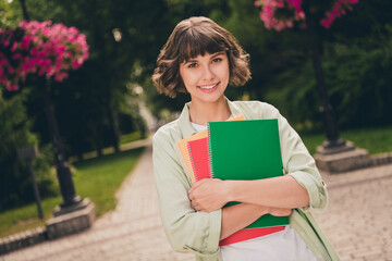 Wall Mural - Photo of charming shiny young woman wear green shirt rucksack smiling embracing copybooks walking outside city street