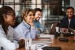 © Maskot - Smiling businesswoman looking away while sitting amidst colleagues at conference table