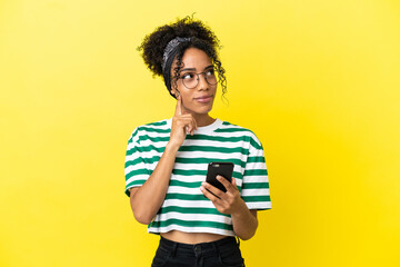 Canvas Print - Young african american woman isolated on yellow background using mobile phone and thinking