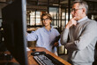 © Maskot - Businesswoman discussing with mature male entrepreneur while standing at desk in creative office