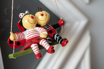 Selective focus shot of a hanging ceramic toy of two happy ladybugs on a swing