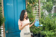 A beautiful young asian woman taking care and watering houseplants by watering can at home