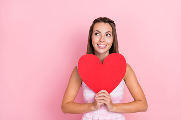 Sticker - Photo of dreamy happy positive young woman look empty space hold heart shape isolated on pink color background