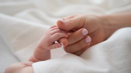 mother holding tiny hand of newborn baby and petting it. parent of adorable infant cares about his c