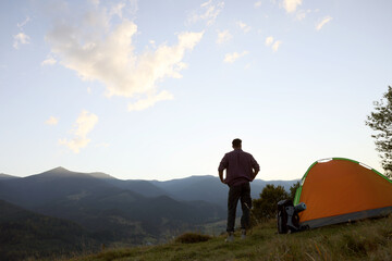 Wall Mural - Tourist with backpack and sleeping pad near camping tent in mountains