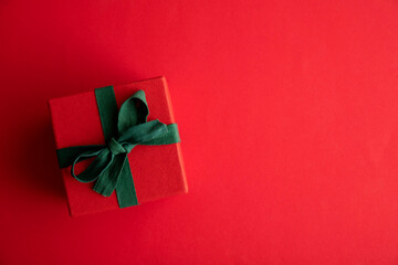 Wall Mural - Festive christmas gift box present tied with a rustic ribbon and bow on a red background. Overhead view