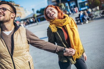 Wall Mural - Smiling couple enjoying on vacation, young tourist having fun walking and exploring city street during the day.