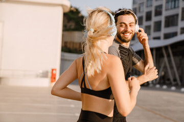 Young man and woman in headphones running together on parking