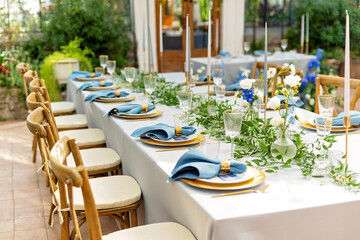 Wall Mural - Banquet wedding table setting with blue napkins, gold cutlery, crystal, fresh flowers and candles. Wedding decorations. Soft selective focus.