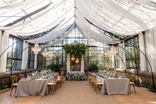 Wedding Banquet Hall In The Greenhouse, Tables Are Set, Decorated With Fresh Flowers, Candles, Crystal Chandeliers. Soft Selective Focus.