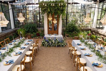 Wall Mural - Wedding banquet hall in the greenhouse, tables are set, decorated with fresh flowers, candles, crystal chandeliers. Soft selective focus.