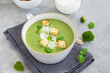 Broccoli cream soup with fresh basil and croutons in a bowl on a gray concrete background. Copy space.