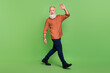 Full body profile side photo of senior cheerful man go walk wave arm hello isolated over green color background