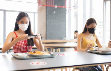 Wall Mural - Young attractive asian teen female influencer, foodie blogger take photo of food  .keep social distance for protect infection from coronavirus covid-19, restaurant and social distancing concept.