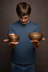 Young handsome tall slim white man with brown hair offering two bowls in blue shirt on grey background