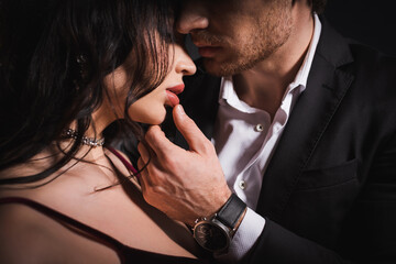 elegant man in black suit touching lips of sensual brunette woman