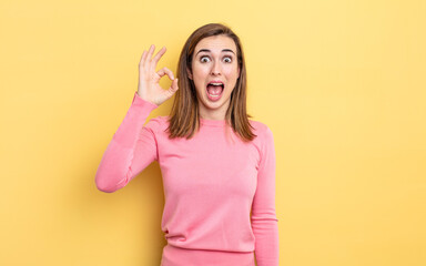 young pretty girl feeling successful and satisfied, smiling with mouth wide open, making okay sign with hand