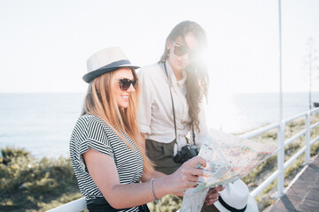 Two beautiful blonde and brunette women with tourist map on holiday