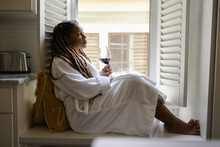 Woman In Bathrobe Sitting By Window, Holding Glass Of Wine