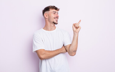 young handsome man smiling happily and looking sideways, wondering, thinking or having an idea