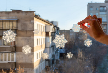 Hand pasting hand-made snowflake stickers on the window of a house, close-up, view from the window.