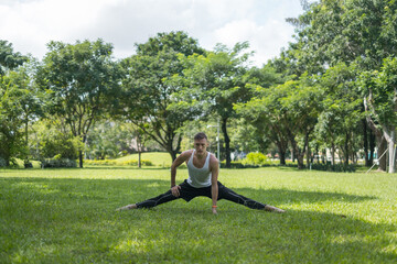 Sporty active young man in sportswear doing sport exercises in the park. Fit caucasian man stretching on the grass outdoors. Healthy lifestyle concept