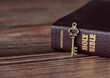 A rustic old vintage retro key with closed Holy Bible book with gold text on a wooden table. A Christian biblical concept of revelation, prayer, faith, and trust in God Jesus Christ. A close-up.