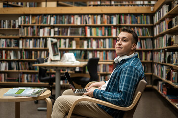 College break. Wireless headphones listening to an audiobook.  Male online education via the Internet on the school's website. The student is in the library.