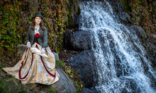 Woman In A 19th Century Suit With An Umbrella Against The Background Of A Waterfall In Autumn