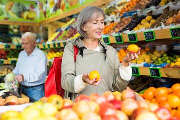 Portrait of adult woman choosing sweet apples and other fruit on counter of farmers market