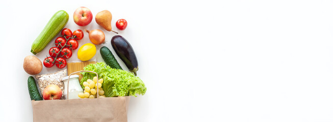 Paper grocery bag with fresh vegetables, fruits, pasta, oatmeal and milk on white table. Food shopping, delivery, diet concept. Healthy food background. Flat lay, top view, copy space, banner.