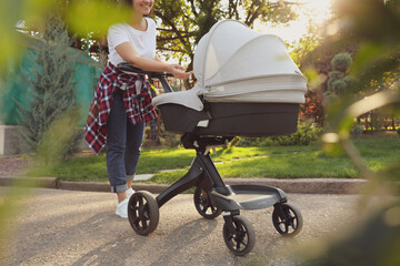 Canvas Print - Happy mother with baby in stroller walking in park on sunny day, closeup