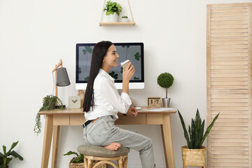 Poster - Young woman with cup of drink at table in room. Home office