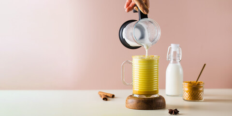 Banner milk froth is poured into a glass with golden latte with turmeric. Moon milk for better sleep. 