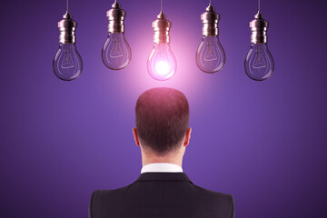 Wall Mural - Back view of young european businessman looking at abstract glowing row of light bulbs on purple background. Idea, solution and innovation concept.