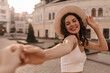 © Look! - Close-up of wonderful pretty caucasian young girl shyly smiles stretching out her hand to someone forward. Fair-skinned brown-haired woman holds beige hat on her head in white top.
