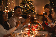 © Syda Productions - holidays and celebration concept - multiethnic group of happy friends with sparklers having christmas dinner at home