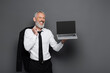 © LIGHTFIELD STUDIOS - happy middle aged businessman in suit holding laptop with blank screen and blazer on grey