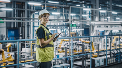 Poster - Female Car Factory Engineer in High Visibility Vest Using Laptop Computer. Automotive Industrial Manufacturing Facility Working on Vehicle Production with Robotic Arms. Automated Assembly Plant.