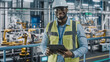 Portrait of Automotive Industry Engineer in Safety Uniform Using Tablet at Car Factory Facility. Happy Assembly Plant African American Man Specialist Working on Manufacturing Modern Electric Vehicles.