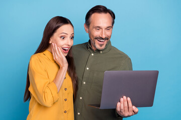 Poster - Photo of amazed cheerful happy people look shocked hold computer news isolated on blue color background