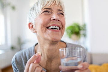 Head shot portrait happy woman holds pill glass of water, takes daily medicine vitamin D, omega 3 supplements, skin hair nail strengthen and beauty, medication for health care concept