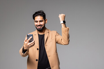 Wall Mural - Portrait of a happy satisfied indian man looking at mobile phone and shouting isolated over white background