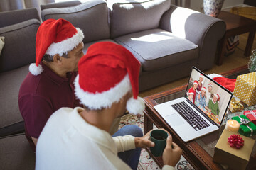 Poster - Biracial father and adult son in santa hats making christmas laptop video call with family