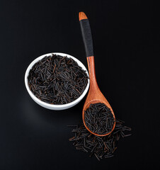 Black rice in a white bowl with a wooden spoon on a black background. Top view