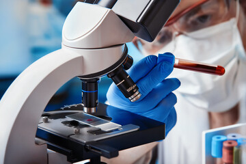 microscopist scientist examining a blood sample under a microscope infected with covid-19 in the lab